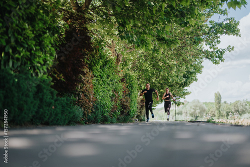 Wallpaper Mural Two individuals jogging together on a shaded pathway surrounded by lush green trees, promoting fitness, healthy living, and enjoying nature on a beautiful day in the park. Torontodigital.ca