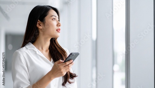 スマートフォンを手に持って、窓の外を見ながら考え事をしてる女性のイメージ。
