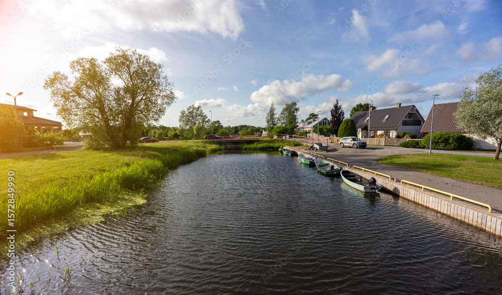 Fototapeta premium Calm river with moored boats, surrounded by greenery.