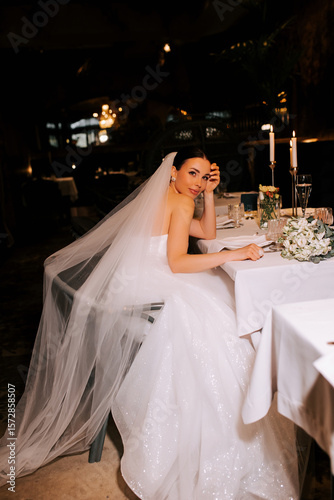 Obraz na plátně Bride in elegant gown sits at candlelit table during evening reception celebrati