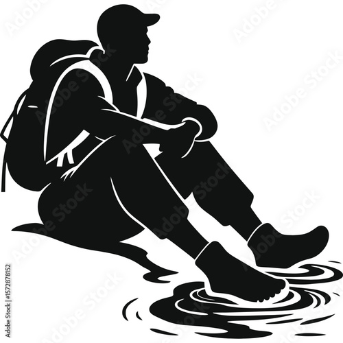 A silhouette of a hiker sitting with a backpack and dipping their feet in water on a sunny day outdoors