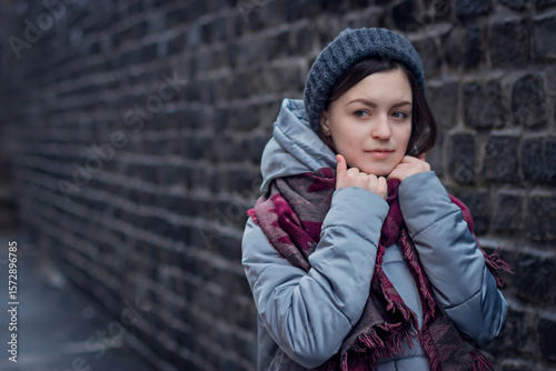 Sad girl stands near a brick wall in jacket hat and scarf