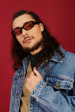 Stylish young man with a beard posing against a vibrant red backdrop in casual attire