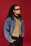Handsome young man with beard poses confidently in stylish outfit against bold red backdrop