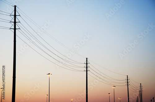 Powerlines and light poles against clear sky at dusk