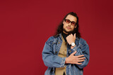 Handsome young bearded man poses confidently against a vibrant red backdrop showcasing his style