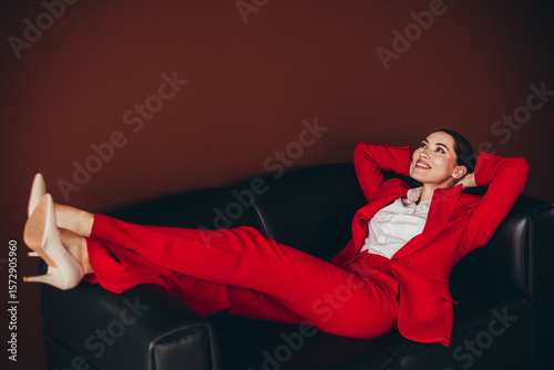 Fotografie Attractive Confident Businesswoman in Red Suit Reclining on a Black Sofa Display