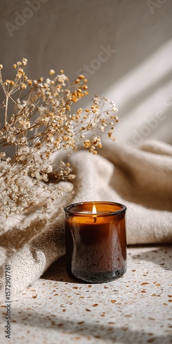 A lit candle in a glass jar with dried flowers creates a warm and inviting ambiance