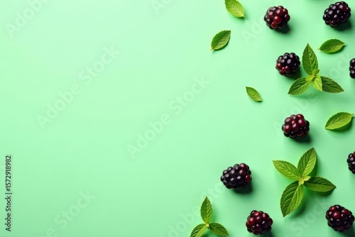 A vibrant arrangement of fresh blackberries and aromatic mint leaves on a light green background provides a refreshing visual