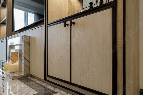 Detail of a custom built-in cabinet featuring light wood grain doors with black metal frames and minimalist T-bar handles. Modern, bespoke furniture.