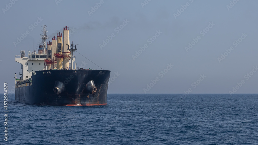 Fototapeta premium A large marine vessel transports cargo on the high seas. Navigation of large ships. A large cargo ship at sea. Smoke is coming out of the chimney of a marine vessel.