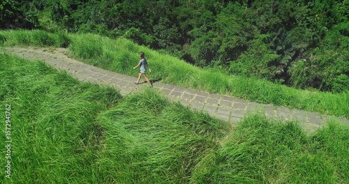 Aerial drone footage of a young woman walking on the Campuhan Ridge Walk in Ubud, Bali, surrounded by lush green vegetation and enjoying the sunny weather