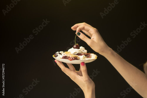 An elegant hand presents a pie topped with whipped cream and a cherry, creating an inviting scene that showcases the fusion of art and culinary delight in a stunning composition.