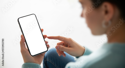 Woman holding and pointing at smartphone with blank screen, over shoulder view of person using mobile phone with empty display mockup