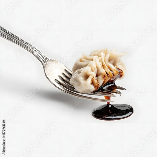 Delicious dumpling on a fork dripping with savory sauce against a clean white background