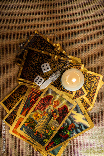 Tarot cards with vivid illustrations lie on burlap, with a quartz pendulum and a lit candle. A mystical setup evoking divination, fortune-telling, and spiritual ritual themes.