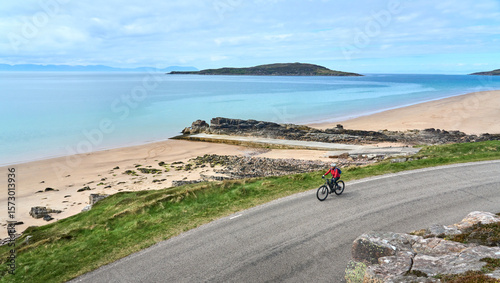 cheerful senior woman riding her electric mountain bike at a rocky beach of the scottiish Atlantic coast near Gairloch, Scotland, UK