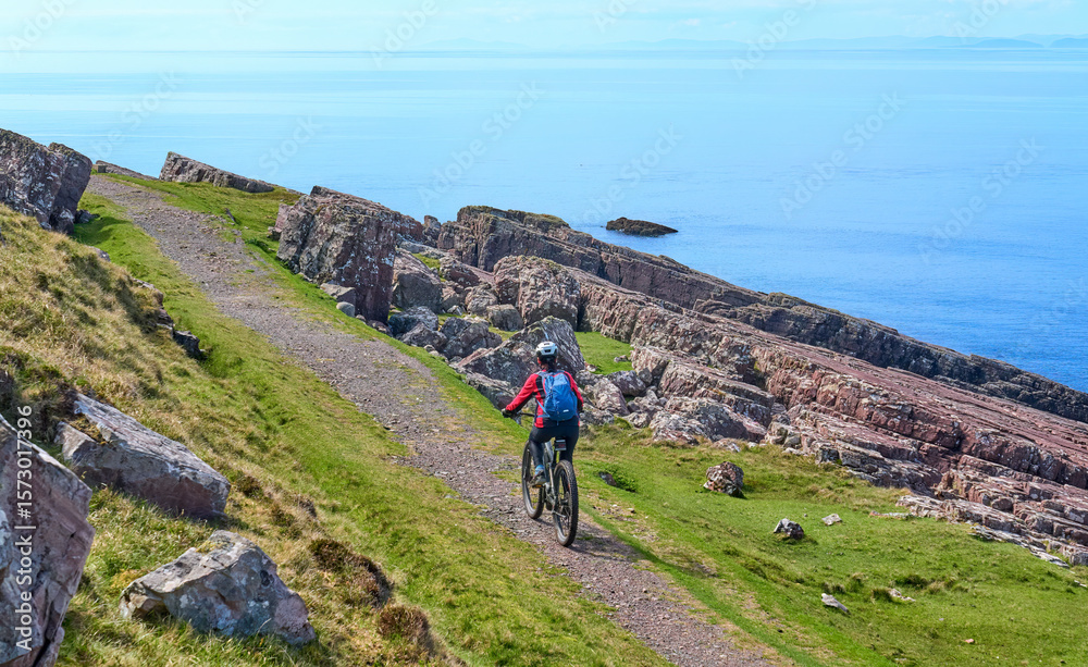Obraz premium active senior woman riding her electric mountain bike on the cliffs near Rua Reidh Lighthouse next to Gairloch in north western Scotland, UK