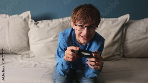  preteen boy with glasses with a joystick playing video game console sitting on the couch at home.  Generation Z.  gambling addiction