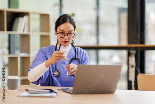 Female medical intern in blue medical scrubs e-learning on laptop computer at the ordination, Doctor and nurse healthcare and medicine.