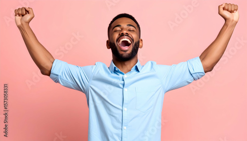 Joyful Black Man With Raised Arms in Light Blue Shirt Against Pink Background