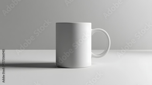 A clean, minimalist white mug stands on a desk with a blank, light gray background. The simple design and neutral colors make it ideal for product mockups and branding.
