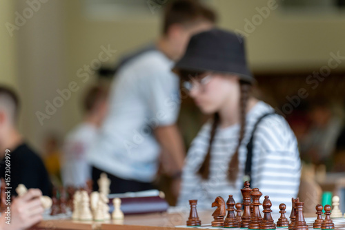 A young woman in glasses concentrates on a move while playing chess. A girl plays in a chess tournament.  Girl at the chessboard. Tournament, portrait of teenage girl playing chess	
