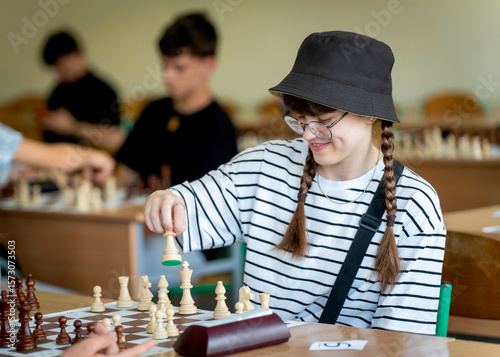 A young woman in glasses concentrates on a move while playing chess. A girl plays in a chess tournament.  Girl at the chessboard. Tournament, portrait of teenage girl playing chess	