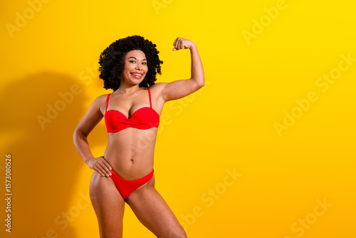 Confident woman in red swimsuit posing against a vibrant yellow background, emphasizing strength, beauty, and self-assurance.