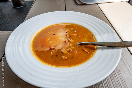 Frankfurter soup (red pepper broth with sliced sausage and potato) in white plate .