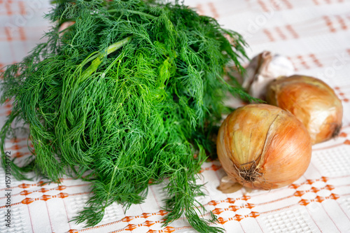 Bunch of dill, two onion and garlic on table.