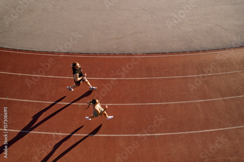Two athletes running on track from above with long shadows