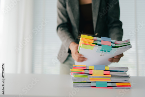 Young female employee is working with a pile of documents to search for information and check documents on the table. Document search concept.