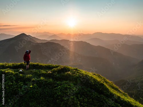 Aerial view of man on top of a mountain at sunset with mountain range in the background. Achenkirch, Tirol, Austria