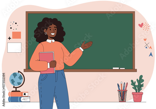 A smiling Black female teacher stands in front of a classroom blackboard, holding a book and gesturing to the board.