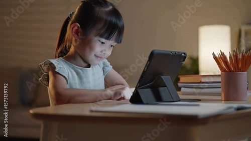 Asian student girl using tablet computer, studying online at home at night