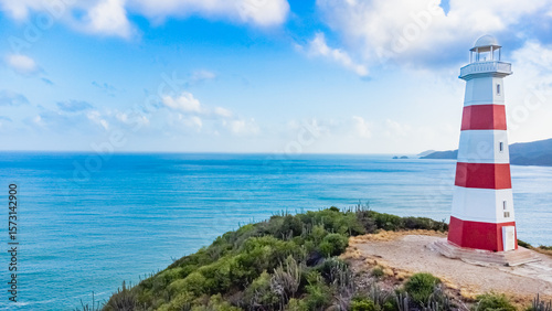 Red and white lighthouse is on a rocky cliff overlooking the ocean