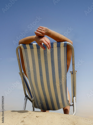 Woman sunbathing on deckchair on the beach shot against blue sky