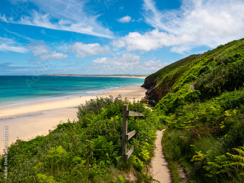 The South West Coast Path, passes Carbis Bay, Cornwall, UK, along scenic views of the bay, sandy beach and coastline. Blue sea, bright sky.