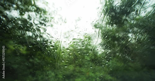 Rain droplets running down a parked car's windshield. Moody close up, wide angle view, real time, shallow depth of field, blurred nature bokeh background, no people