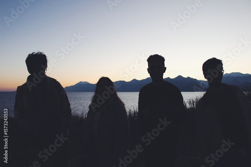 Four young adults silhouettes during sunset over seascape