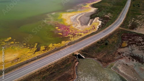 A breathtaking aerial view showcases a winding road by the vibrant and colorful lake shoreline