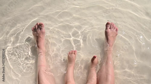 Top view of the legs of a one year old boy and his mother on the seashore. 