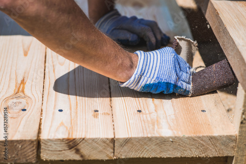 A carpenter wearing cloth gloves manually polishes wooden boards with sandpaper for grinding. The concept of DIY woodworking and construction.
