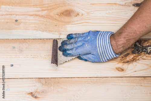 A carpenter wearing cloth gloves manually polishes wooden boards with sandpaper for grinding. The concept of DIY woodworking and construction.