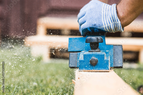 A hand-held electric planer in the hands of a craftsman. A man planing boards with an electric tool. Production of wooden products. Construction, wood processing.