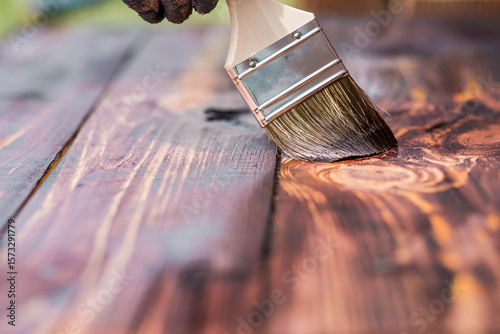 The procedure for protecting and coating wooden boards. A worker applies a protective wood stain with a brush. The process of restoring a hardwood flooring.