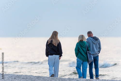 Fototapeta Naklejka Na Ścianę i Meble -  Three persons family walking on a sandy beach of Baltic Sea during sunset.