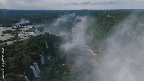 Aerial view Iguazu Falls reveals vast panorama of rainforest and winding river. Numerous waterfalls drop into canyon Mist rises above trees while landscape shows impressive scale of this destination
