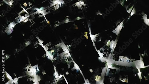 Aerial view displays residential district of Bukhara, Uzbekistan, at night. Modern street lights create glowing lines among dark rooftops, showing the geometry of city blocks and quiet living spaces.
